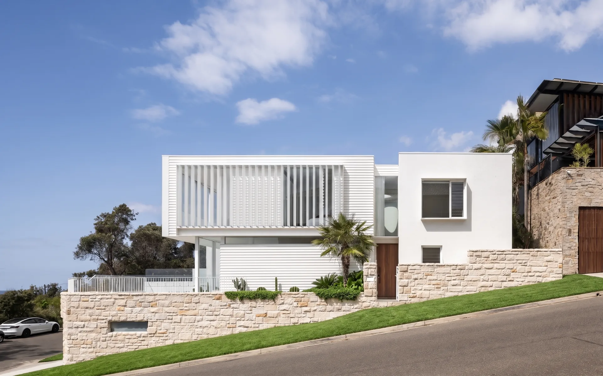 Coastal residence with white slatted facade and sandstone wall